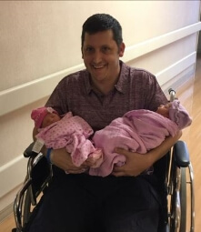 father in wheelchair holding twin girls